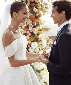 a bride and groom holding hands in front of a floral arch at their wedding ceremony