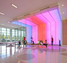 people are sitting on benches in a large room with bright lights and windows, while one person is using a laptop