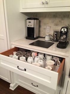 an open drawer in a kitchen filled with coffee cups and other items on the counter