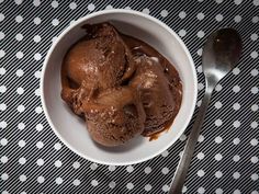 two scoops of chocolate ice cream in a bowl with spoon on the tablecloth