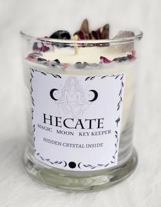 a candle that is sitting in a glass jar on a white tablecloth with the label hecatee magic moon key keeper hidden crystal inside