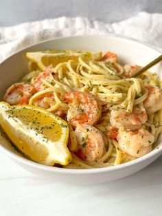 a white bowl filled with pasta and shrimp next to lemon wedges on a table