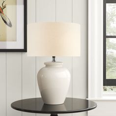 a white vase sitting on top of a black table next to a framed picture and lamp