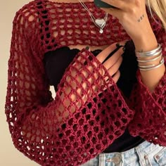 a woman is wearing a red crocheted shawl and holding a cell phone