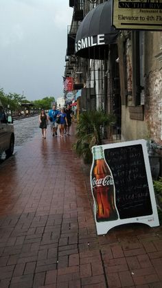 there is a sign on the side of the street that says smile and people are walking down the sidewalk