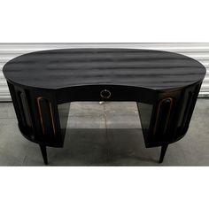 an oval shaped black table with two drawers on one side and a gold ring at the top