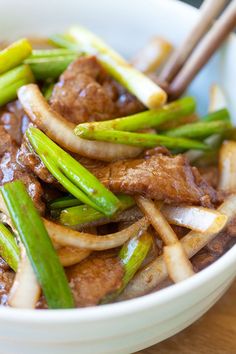 beef and asparagus stir fry in a white bowl with chopsticks on the side