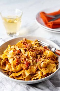 a white bowl filled with pasta and meat on top of a table next to two glasses