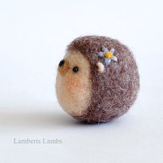 a needle - felted bird with a flower on its head sits in front of a white background