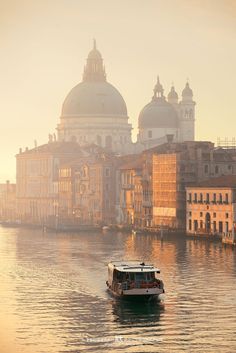 a boat is on the water in front of some old buildings and domed domes at sunset