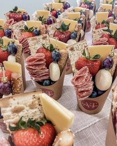 many different types of cheese and fruit in small cups on a table with linens