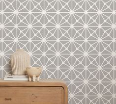 a white vase sitting on top of a wooden dresser next to a wallpapered wall