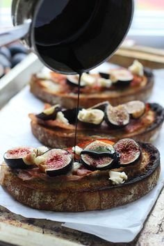 someone is pouring sauce on some bread with figs