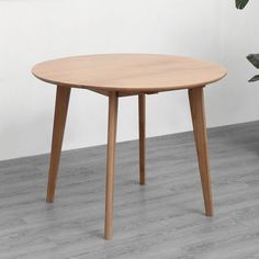 a round wooden table sitting on top of a hard wood floor next to a potted plant