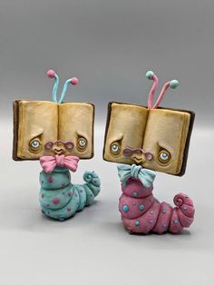 two small figurines are sitting next to each other on a white surface and one has a book in it's head