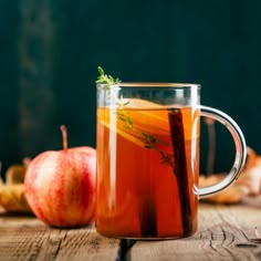 a glass mug filled with liquid next to an apple and leaves on a wooden table