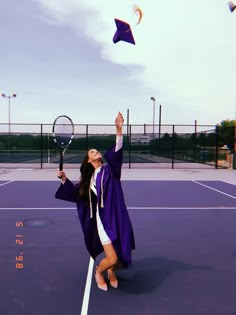 a woman in a graduation gown is on a tennis court with her racquet up