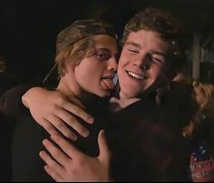 two young men hugging each other in front of a group of people with their arms around one another