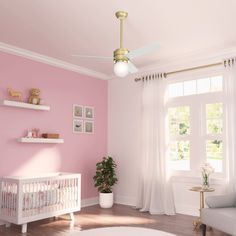 a baby's room painted in pink and white with a gold ceiling fan above the crib