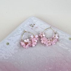 These exquisite hoop earrings feature delicate cherry blossom sakura flowers, available in either pink or white hues.  Each earring is meticulously handcrafted and the ear hoops are plated with  14K gold, exuding elegance and charm.  Perfect for adding a touch of whimsy and sophistication to any outfit, these earrings are versatile enough to be worn as bridal accessories or to elevate everyday looks with a dash of kawaii (cuteness). Small Hoop Pink Flower Earrings, Pink Hoop Flower Earrings For Pierced Ears, Spring Flower Hoop Earrings For Pierced Ears, Spring Pink Hoop Earrings, Pink Hoop Flower Earrings For Spring, Spring Hoop Earrings With Flower Charm As Gift, Spring Flower Charm Hoop Earrings As Gift, Pink Flower Hoop Earrings For Spring, Delicate Hoop Earrings With Flower Charm