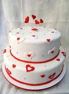 a three layer white cake with red hearts on the top and bottom, sitting on a white tablecloth