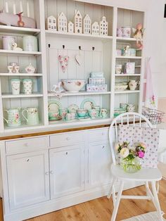 a white chair sitting in front of a shelf filled with dishes