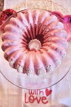 a pink bundt cake sitting on top of a glass plate next to a white table cloth