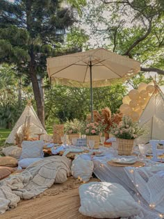 an outdoor picnic setting with pillows, umbrellas and other items on the ground in front of trees