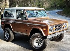 an old ford bronco is parked on the side of the road in front of some trees