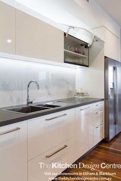 a modern kitchen with stainless steel appliances and white cabinetry, along with hardwood flooring