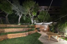 a wooden bench sitting in the middle of a lush green yard at night with lights on