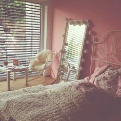 a bedroom with pink walls and white furniture in front of a large window that has blinds on it