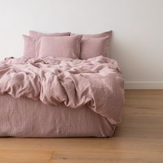 an unmade bed with pink linens and pillows on top of it in a white room