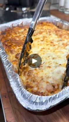 a person cutting into a pizza in a pan on top of a wooden table with tongs