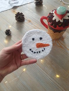 a hand holding a small snowman coaster next to an ice cream cone with a cupcake on it