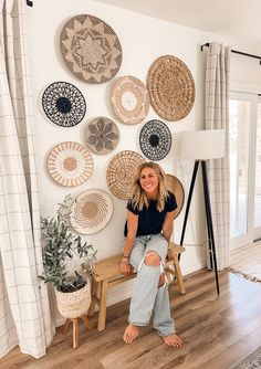 a woman sitting on a bench in front of a wall with woven baskets and plants