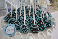 chocolate covered cake pops are on a white platter with blue and brown striped lollipops