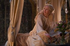 a woman sitting on top of a bed next to a table with flowers in it