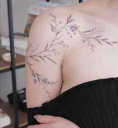 a woman wearing a black dress with purple flowers on her arm and shoulder, showing off her tattoos