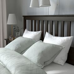 a bed with white pillows and two lamps hanging over the headboard in front of it