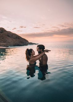 a man and woman are in the water at sunset with their arms around each other