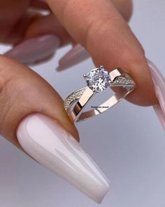 a woman's hand holding a white manicured nail with a diamond ring on it