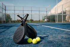 two tennis balls and a racket laying on the court with net in the background