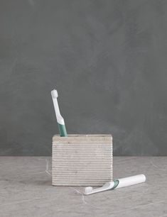 two toothbrushes in a wooden holder on a table next to a gray wall