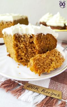 a piece of carrot cake with white frosting on a plate next to a fork