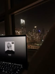 an open laptop computer sitting on top of a window sill in front of a city skyline