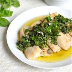 a white plate topped with meat and greens next to a bowl of sauce on a table