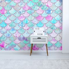 a room with pink, blue and green mermaid scales on the wall behind a white dresser