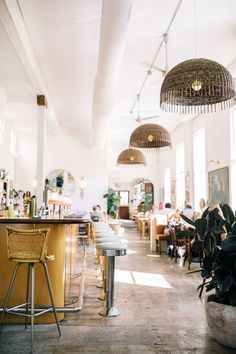 an empty restaurant with people sitting at tables and hanging lights above the bar, in front of large windows