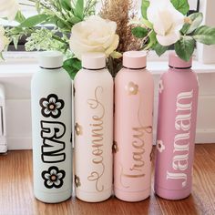 three different colored water bottles sitting next to each other on a wooden floor with flowers in the background